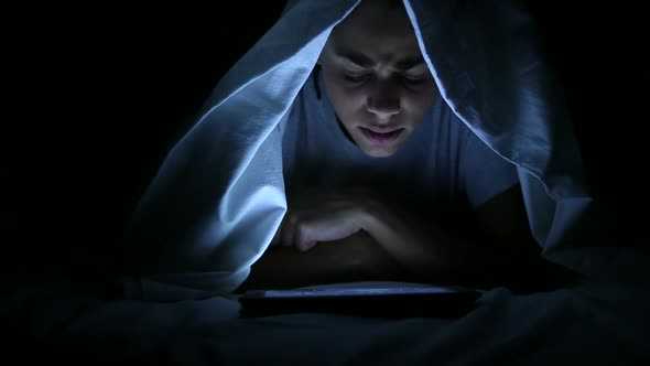 Woman Watching Horror Movie on Digital Tablet under Bed Sheets