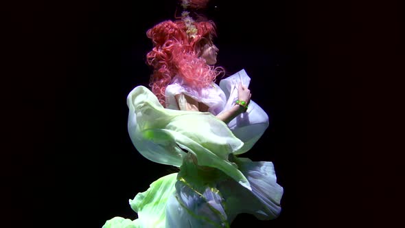 Oceanic Fairy with Pink Hair Dressed in White Gown Is Moving in Depth of Water in Darkness