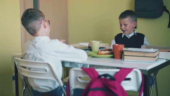 Happy Schoolkids Talk Sitting at Table with Lunch and Books