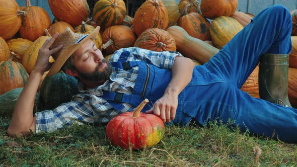 Farmer Rests Near Mound of Pumpkins