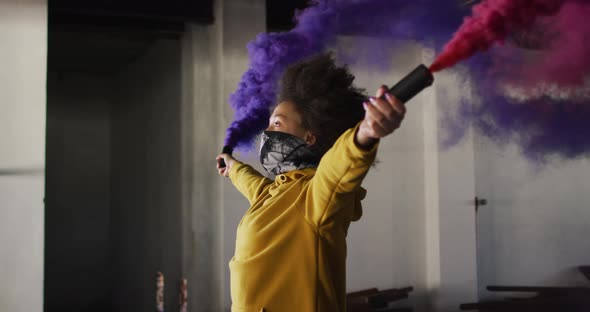 Mixed race woman holding blue and purple flares standing in an empty building