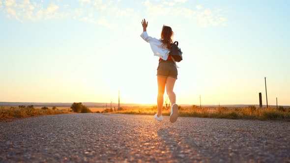 Silhouette From Back of Teenage Girl Who is Waving Her Arms and Running Along an Road in Field