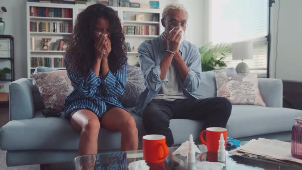 Mixed Race Young Couple Sneezing Noses Suffering From Headache in Living Room