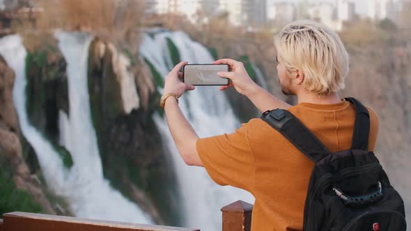 A Young Blonde Man Shoots a Waterfall on His Phone