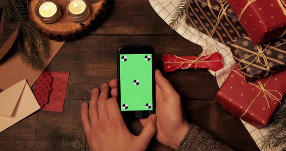 Top View of Male Hands Holding and Using Stylish Smartphone with Green Screen Vertically on Wooden