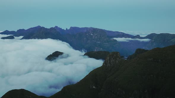 Drone view of clouds flowing down mountain plateau to lower valley