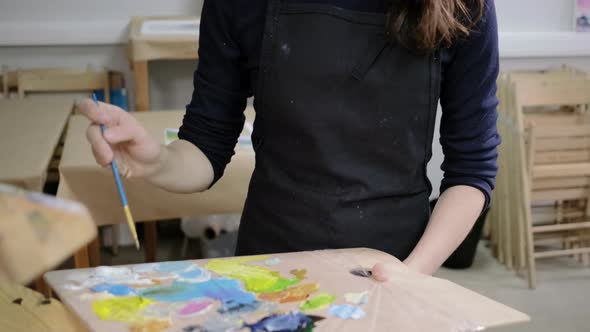 Woman with Apron on Her Body Is Drawing on Easel in Art Workshop