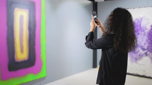 Brunette Girl Is Photographing Modern Picture in Hall of Art Museum Using Phone