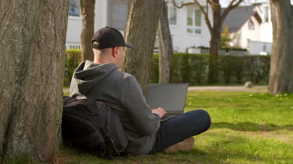 Young Man is Sitting in a Park in a Tourist Place Working on a Laptop