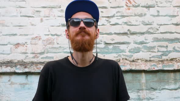 Portrait of young red bearded man in black t-shirt and snapback in rock style on urban background