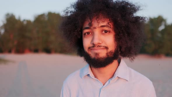 Closeup Portrait of Joyful Young Hispanic Man Curly Hair Standing Alone in Park Smiling and Looking