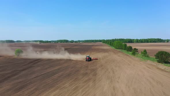 Big red tractor  is cultivating the soil.