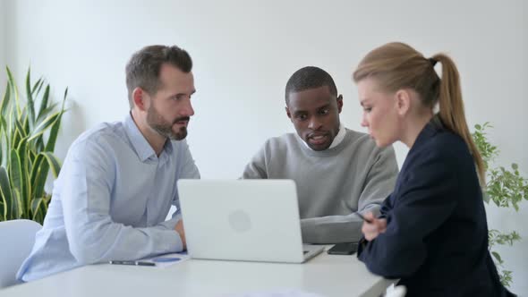 Male and Female Business People Discussing While Using Laptop in Office