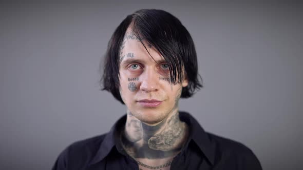 Headshot Portrait of Young Brunette Man with Grey Eyes and Tattoos on Face Looking at Camera