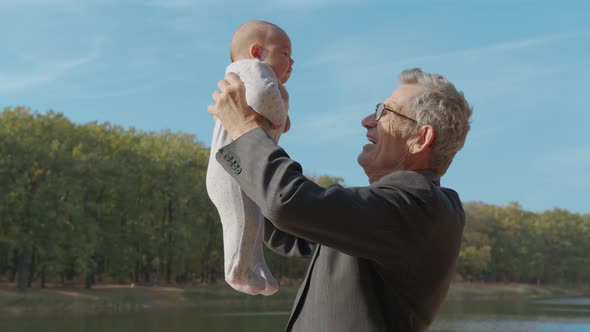 Senior Eldery Man Talking To His Baby Grandson, Holding Him in the Air, Close Up, Side View.