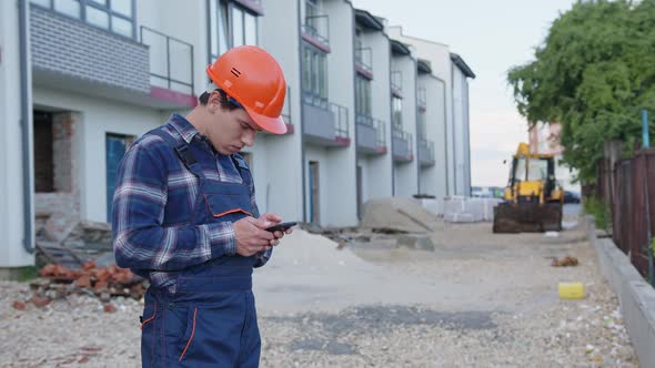 Man Stands and Looks on His Black Phone