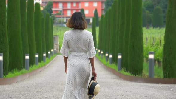 A woman walking on a path with cypress trees while traveling at a luxury resort in Italy, Europe