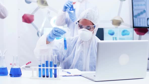 Female Scientis Holding a Test Tube with Smoking Blue Fluid and Writing Formula