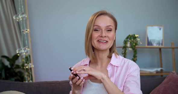 Cheerful Young Woman Talking and Showing To Camera Cosmetic Palette While Sitting on Sofa at Home