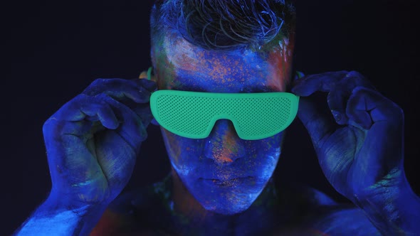 A Man with Fluorescent Drawings on His Body Puts on Green Glowing Disco Glasses