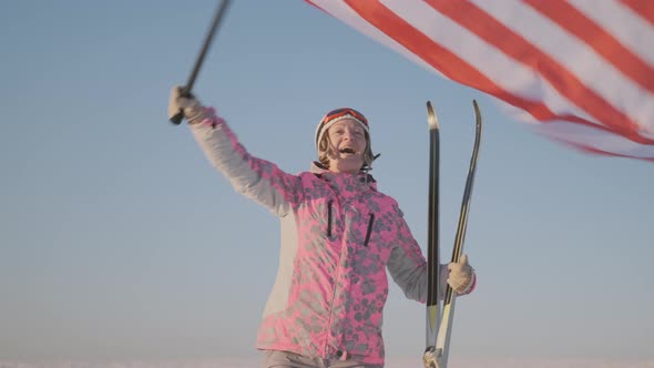 Happy skier woman with skis rejoices waving US flag on background of clear blue sky