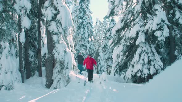 Two Male Hikers With Hiking Poles Snowshoe Through Fresh Winter Snow