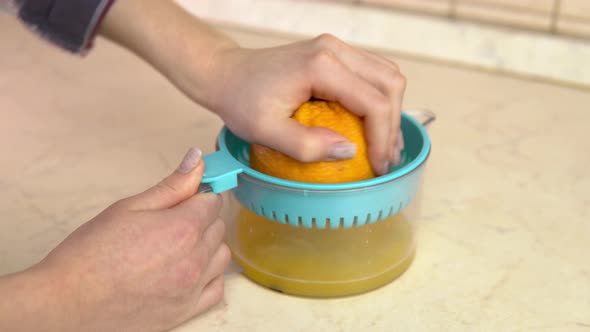 A Woman Squeezes Juice From an Orange. A Woman Uses a Juicer. Hands Close Up.