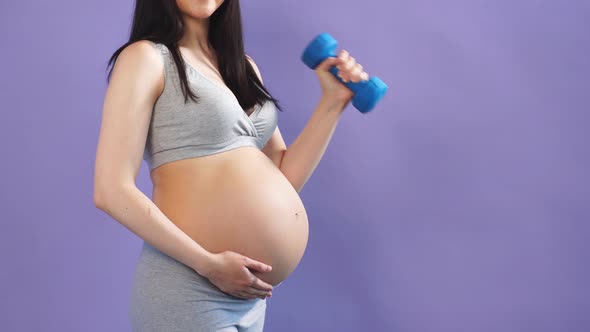 Happy Pregnant Mom Exercising at Studio with Dumbbells on Violet Background