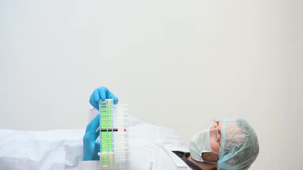 Vertical Video. A Doctor in a White Coat and Protective Mask Enters the Frame and Shows a Tube