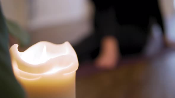 Yoga concept: white candle in the foreground and female doing yoga  in the background. Relax, energy