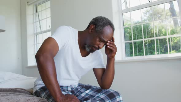 Senior african american man with headache sitting on bed holding head