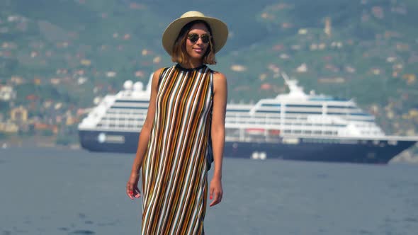 A woman on rocks with a cruise ship traveling in a luxury resort town in Italy, Europe