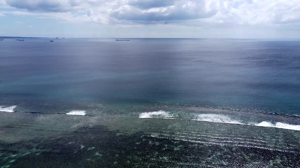 Ocean waves breaking near the shore, with coral reefs and container ship