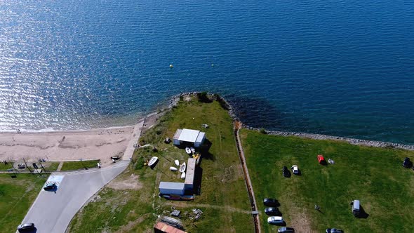 People on the lake with garden to walk, beach and sunbathing area with lawn, boats and parked cars,