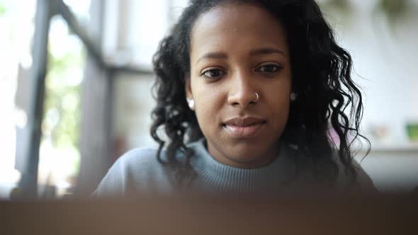 Handsome African woman wearing blue sweater typing by laptop