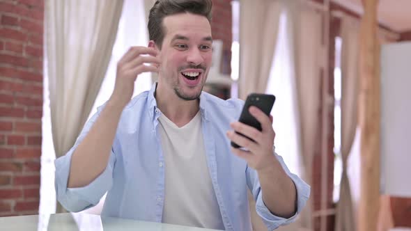 Young Man Celebrating on Smartphone at Home