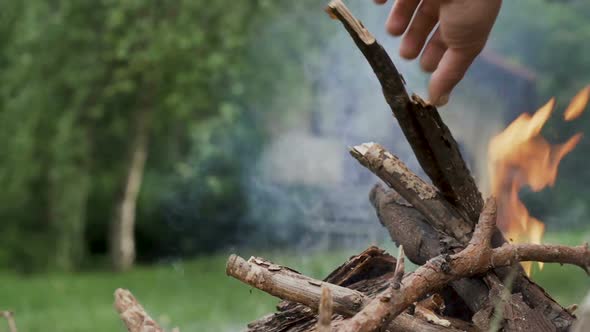 Close Shot of Smoking Bonfire and Hand Putting Wood in The Fire