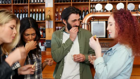 Friends having tequila shot at counter in bar 4k