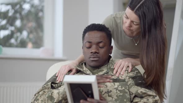 Frustrated Military Man Looking at Picture As Loving Woman Talking Calming Down Spouse