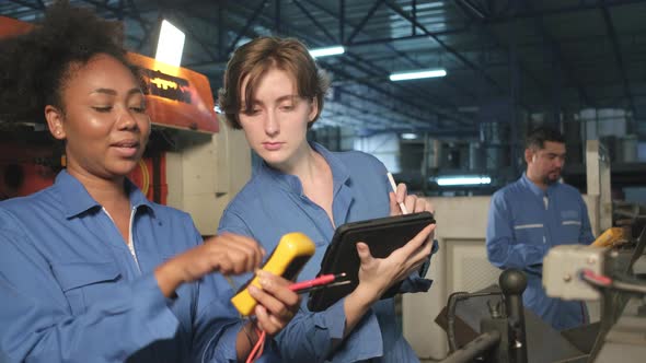 Two professional female engineers inspect machines' electric systems at factory.