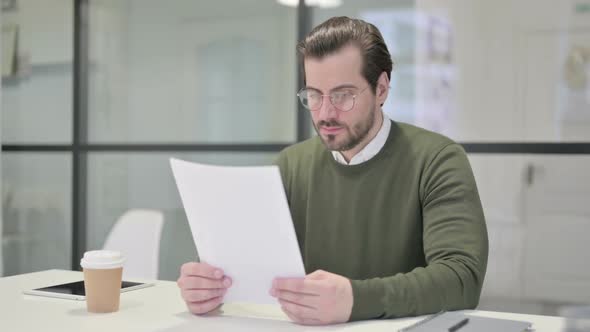 Young Businessman Reading Reports While Sitting in Office