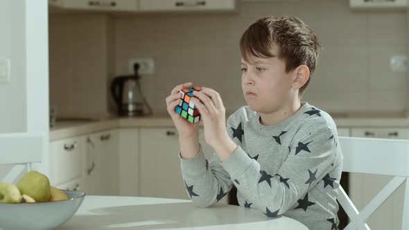 Concentrated boy in grey sweatshirt holding cube and playing with it. 