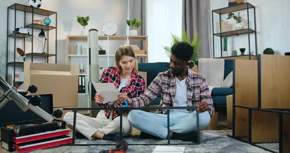 Mixed Race Pair Sitting on the Floor and Measuring Iron Construction with Tape Measure