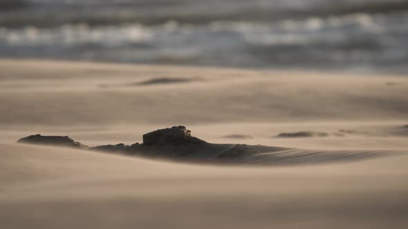 Windy desert weather blowing sand grain past rock formation by rolling waves