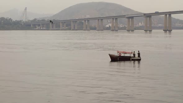 Two Local Men Stand On Small Boat Floating At Guanabara Bay Near Rio Niteroi Bridge In Brazil. - wid