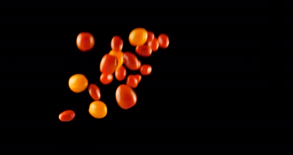 Sweet red ripe cherry tomatoes flying against black background