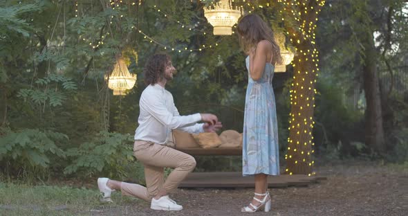 Wide Shot of Loving Romantic Man Standing on One Knee and Proposing To Beautiful Young Woman