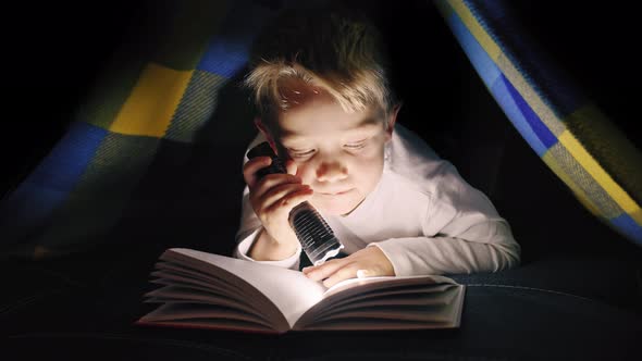 Young Boy Reading a Captivating Book at Night  Lighting with a Flashlight Under the Blanket