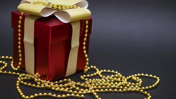 Beautiful Red Gift Box with a Gold Bow and Beads on a Black Background