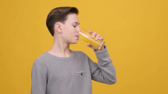 Teen Boy Drinking Orange Juice Smiling To Camera Yellow Background